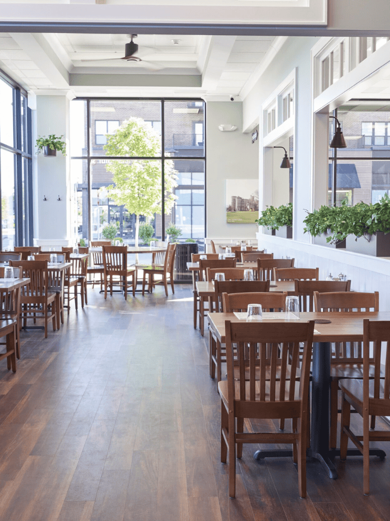 Bright modern restaurant interior with large windows, natural light, and wooden furniture.