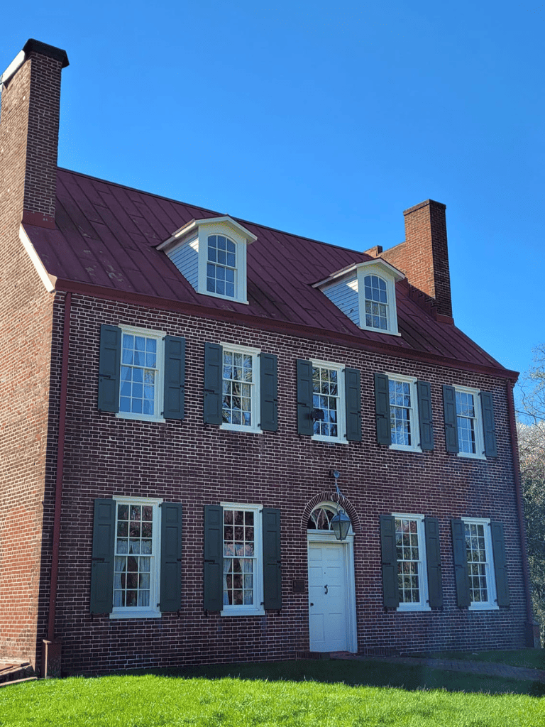 Brick historic house with green shutters and dormer windows under a clear blue sky.