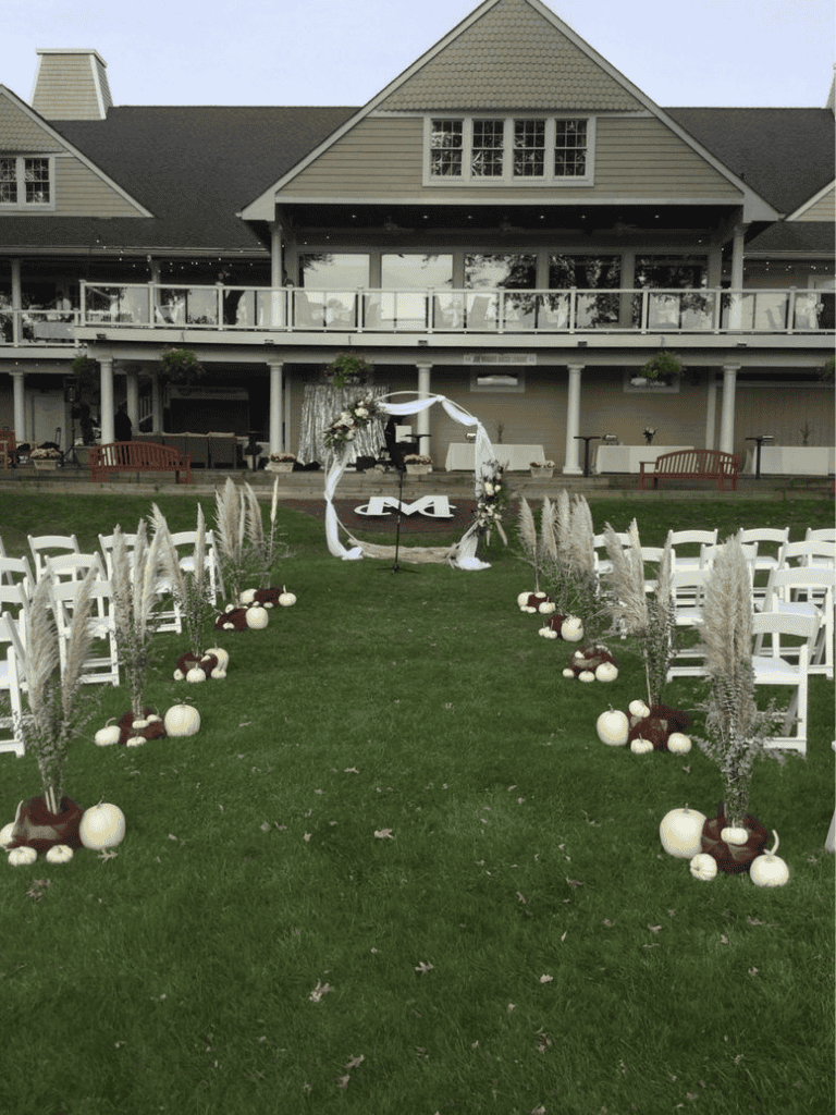 Elegant outdoor wedding ceremony setup with floral arch and pumpkin decorations, hosted on a lush green lawn.