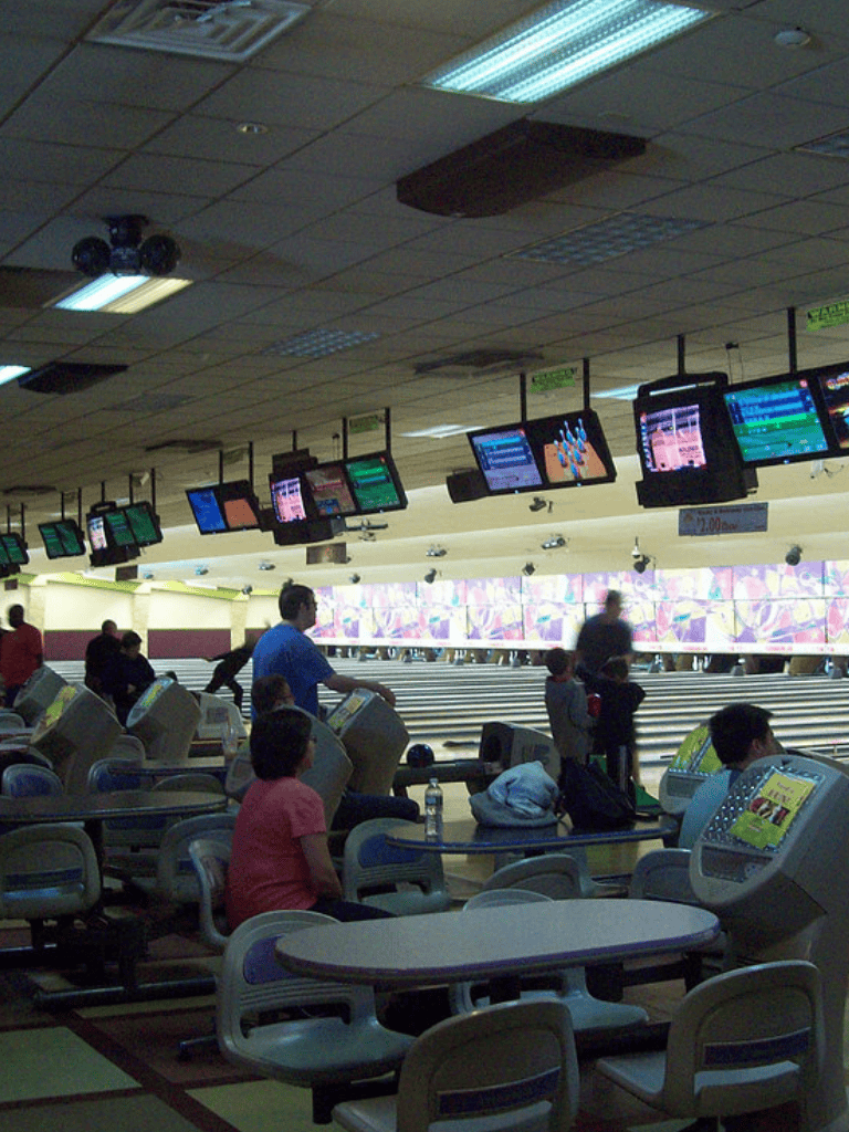 Bowling alley with people playing and digital screens above, indoor recreational entertainment, QuestForDirections logo.