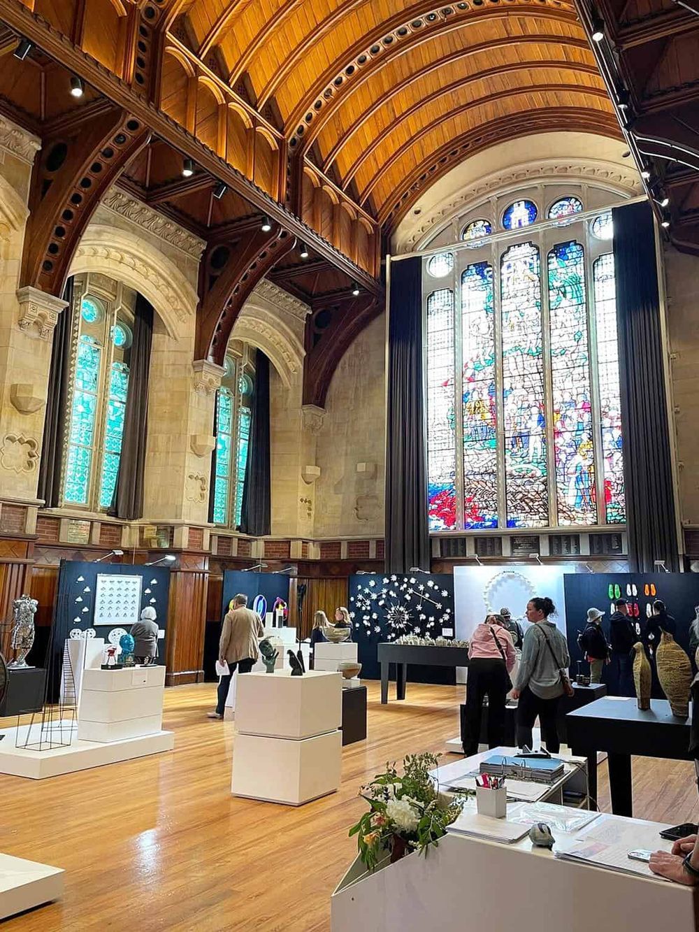 Colorful stained glass window inside a historic church or building with wooden arches and modern art displays.
