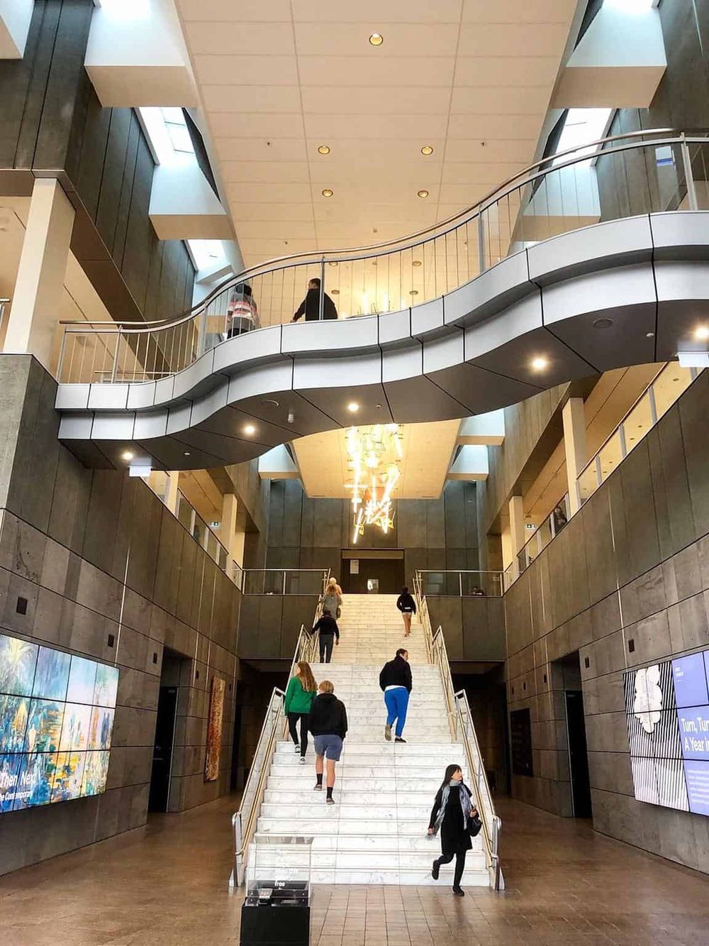 Bright modern lobby with staircase, escalators, and digital displays at QuestForDirections location.