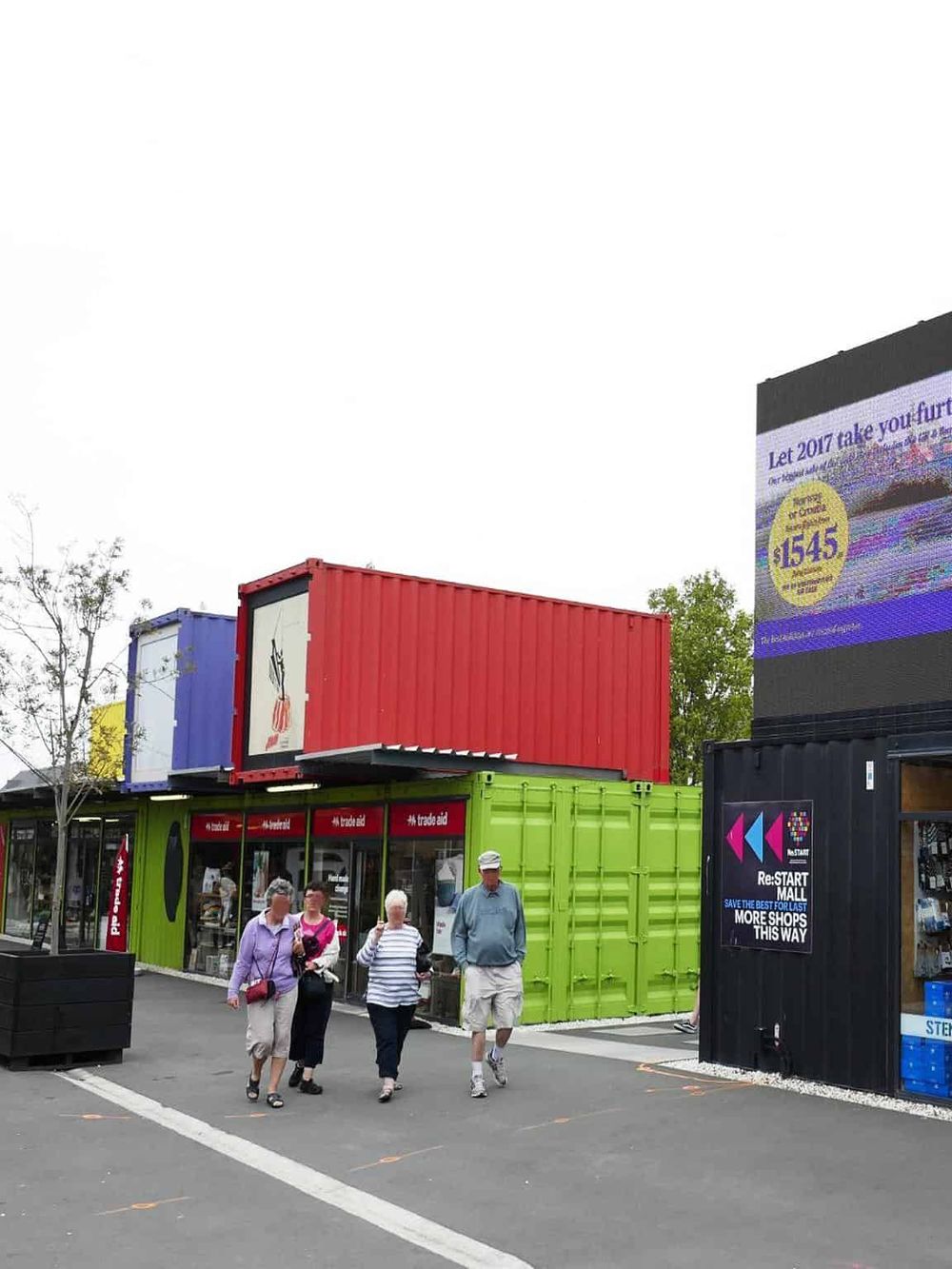 Colorful shipping containers repurposed into retail shops with shoppers walking outside.