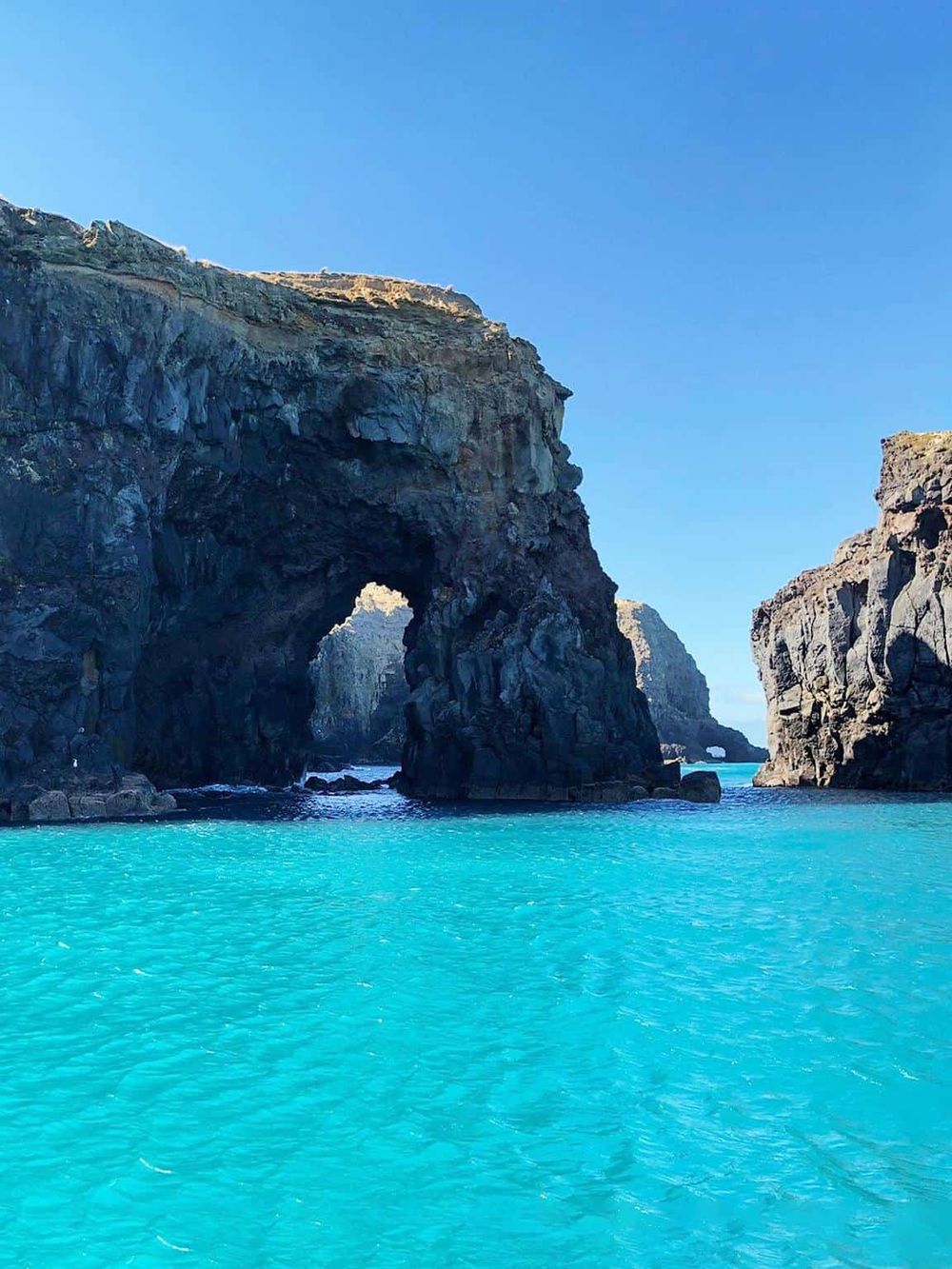 Vivid ocean water and natural rock formations at the coastline under a clear blue sky.