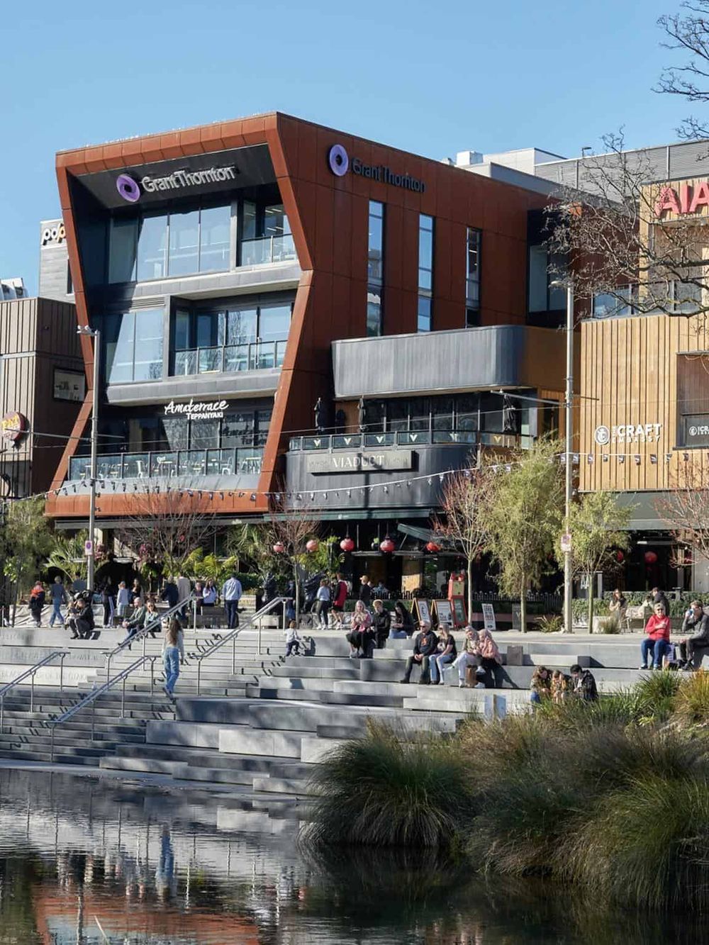 Modern urban shopping mall with Quest for Directions building logo, bustling outdoor activity, and scenic steps and water feature.