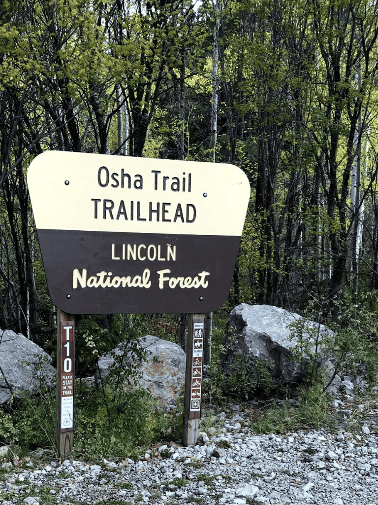 Osha Trailhead sign in Lincoln National Forest, surrounded by forest and rocks.
