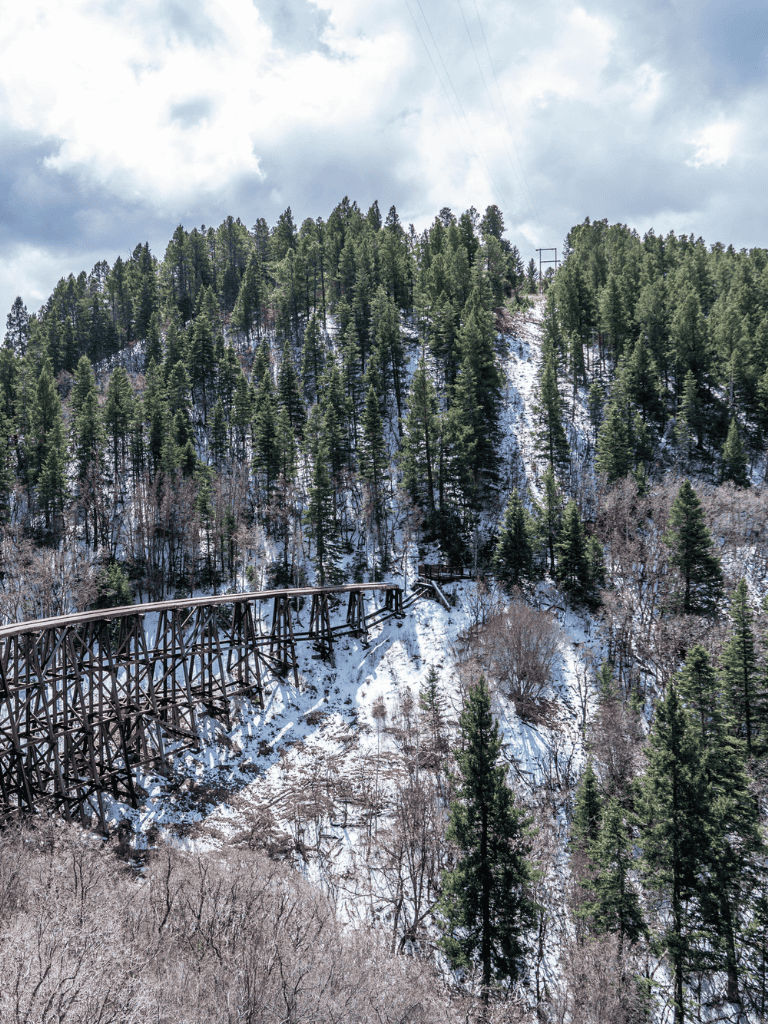 Old wooden train trestle bridge in snow-covered forest landscape.