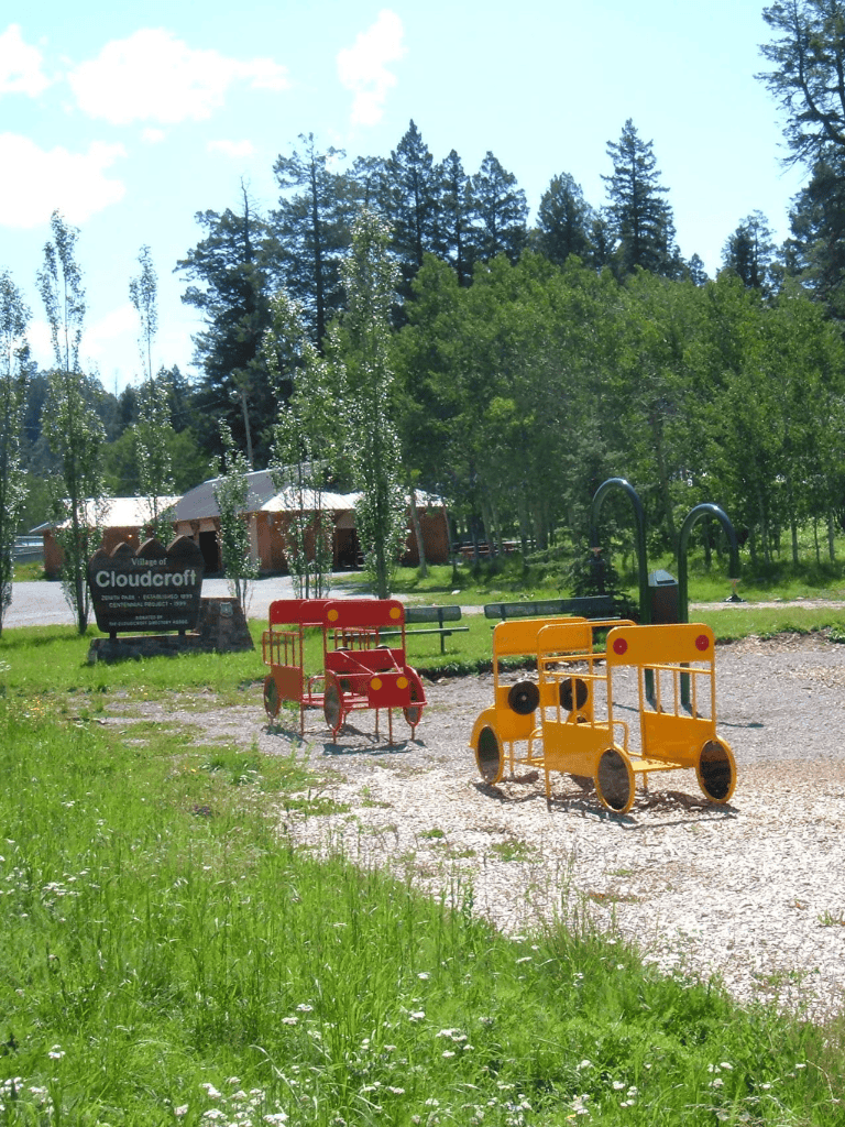 Colorful outdoor children's play equipment in a park surrounded by trees at Cloudcroft village.