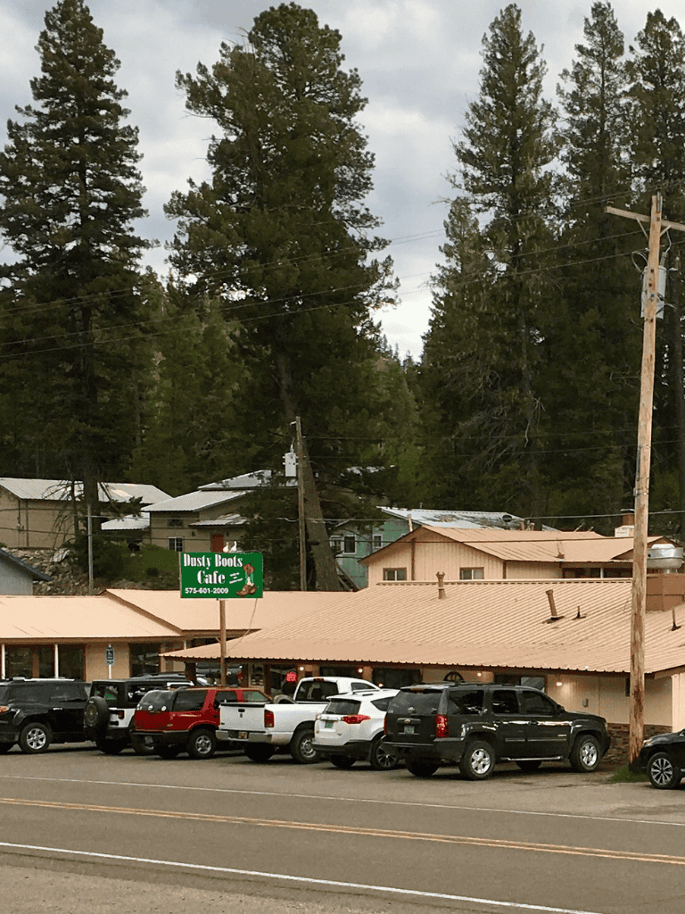 Aerial view of Dusty Boots Cafe surrounded by parked cars and tall pine trees.