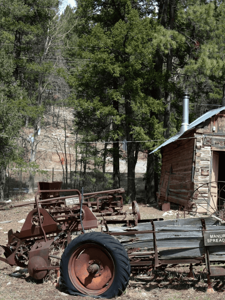 Rusty old farming equipment and a wooden shed in a rural outdoor setting.