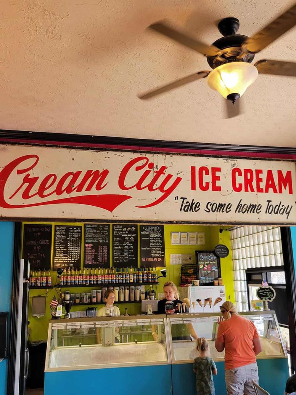 Colorful ice cream shop interior with customers and staff, featuring a bright green wall and menu board.