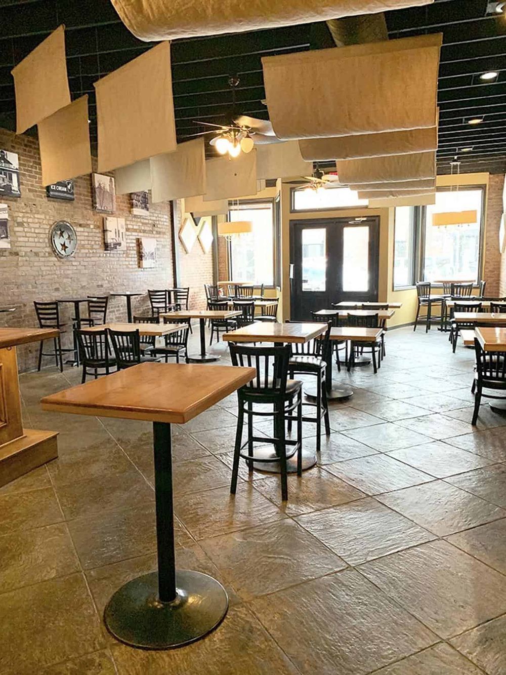 Brightly lit restaurant interior with wooden tables, black chairs, and decorative wall art.