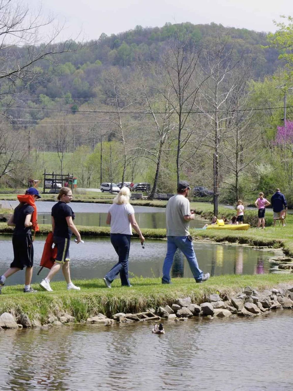 Tranquil outdoor park with people enjoying walking, paddle boating, and scenic mountain views. Perfect for family outdoor activities.