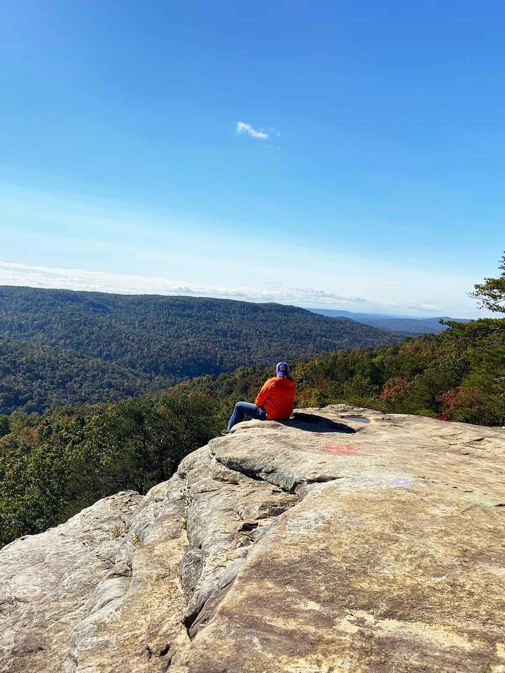 Breathtaking mountain view with a person sitting on a rocky ledge enjoying nature and outdoor exploration.