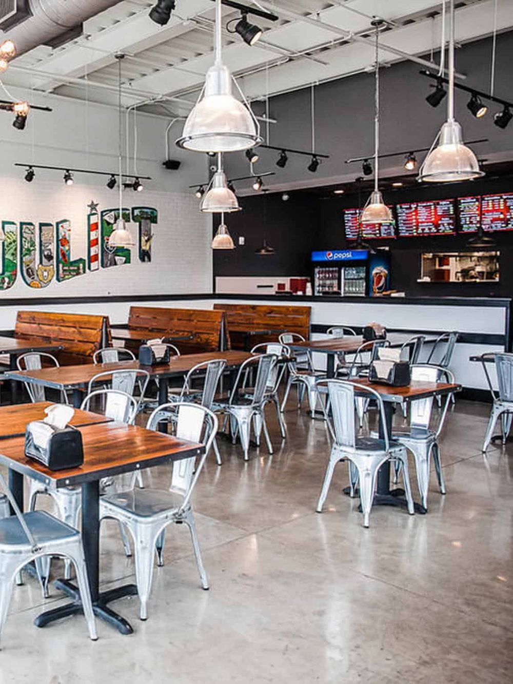Bright modern restaurant interior with wooden tables, metal chairs, and hanging pendant lights, perfect for casual dining.