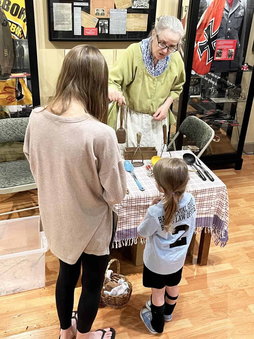 Antique wartime relic display at a museum, with a woman and children observing artifacts.