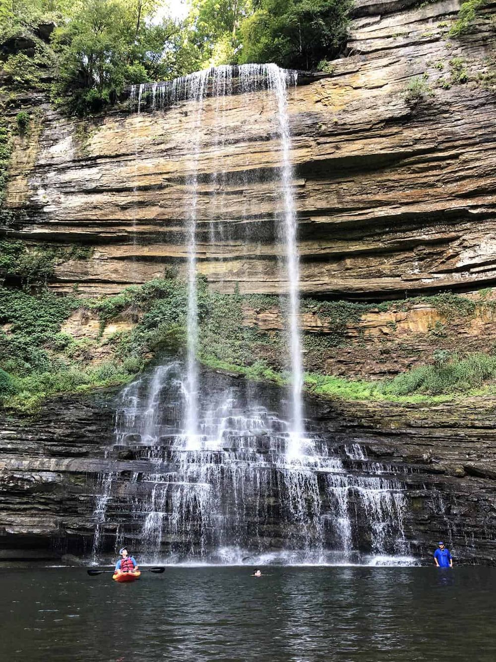Serene waterfall with kayaking and swimming at scenic outdoor location for nature adventure.