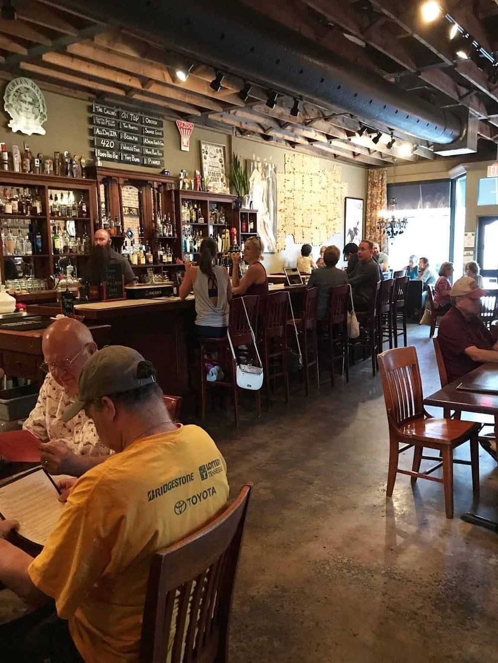 Cozy bar interior with wooden decor, patrons enjoying drinks, and a welcoming atmosphere.