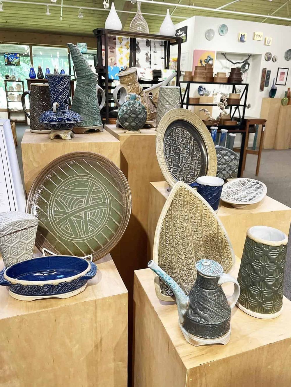 Colorful ceramic pottery and bowls displayed on wooden pedestals in an art gallery setting.