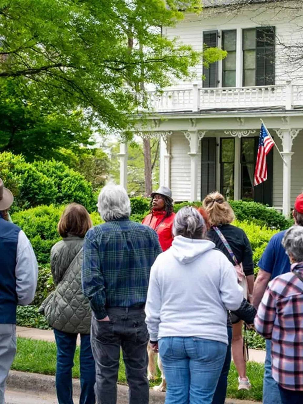 Historic home tour with guided group at a charming Victorian-style house in a lush green neighborhood.