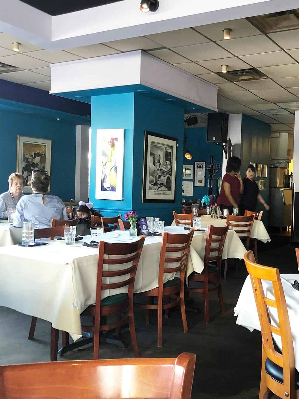 Comfortable restaurant interior with dining tables, artwork, and waiting staff, ideal for a pleasant dining experience.