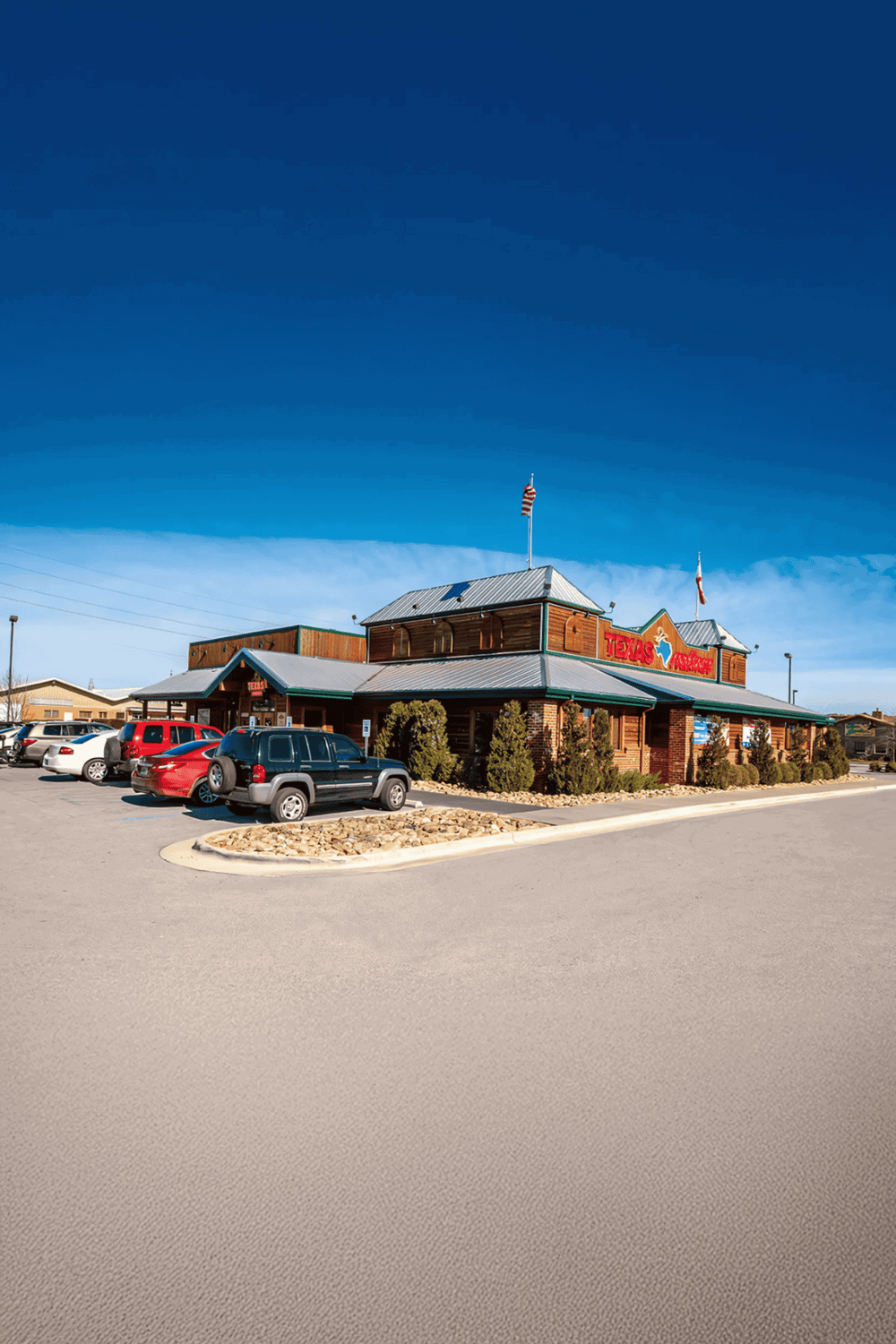 Aerial view of Texas Roadhouse restaurant with parking lot and clear blue sky.