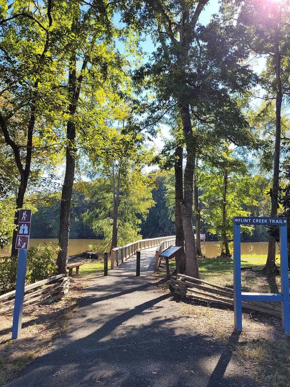 Scenic trail entrance by the river with trees and signage at Flint Creek Trail, perfect for outdoor hiking adventures.
