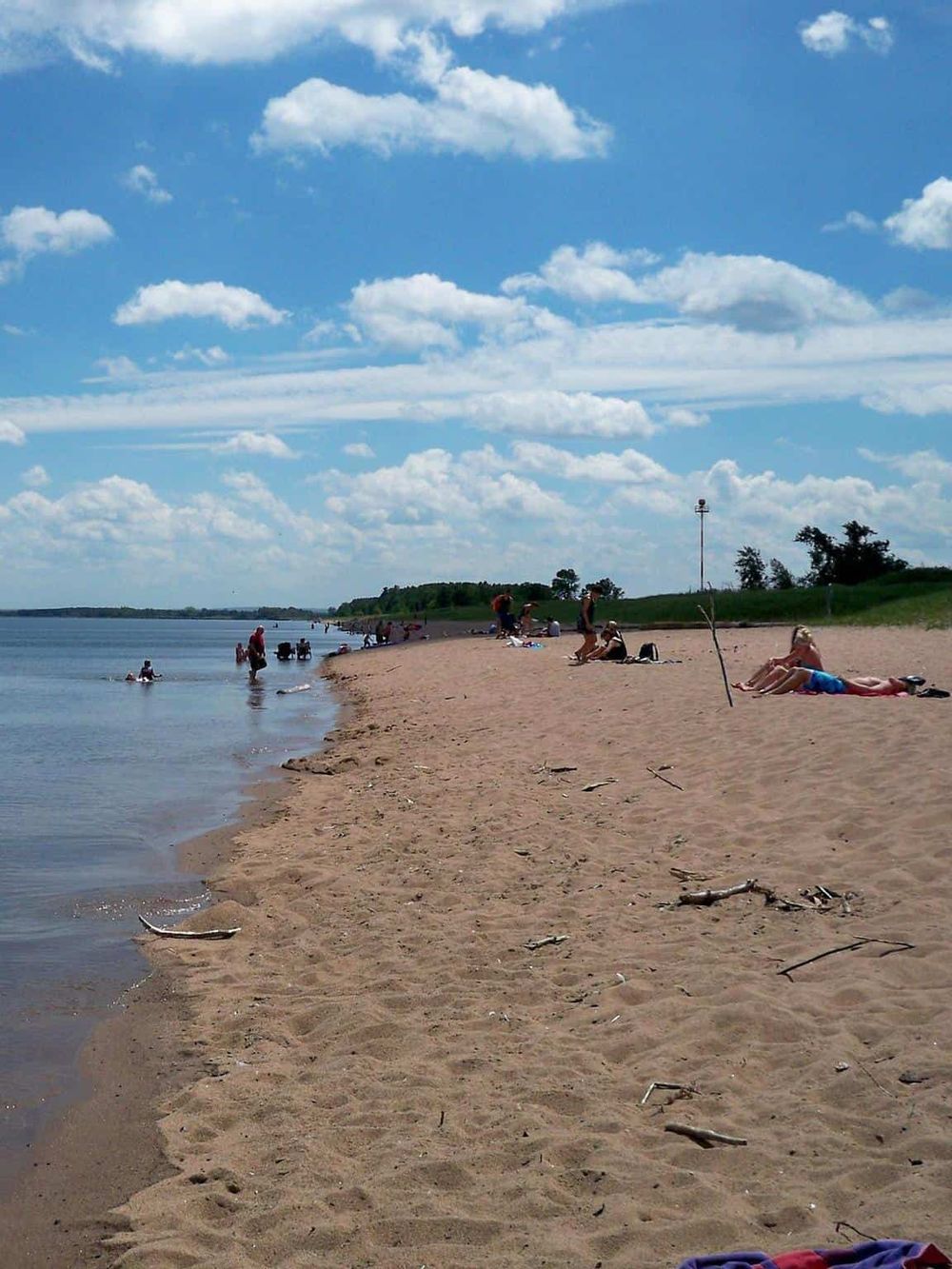 Serene beach scene at a lakeside with people relaxing and enjoying the sunny day, perfect for outdoor adventures and lakeside relaxation.