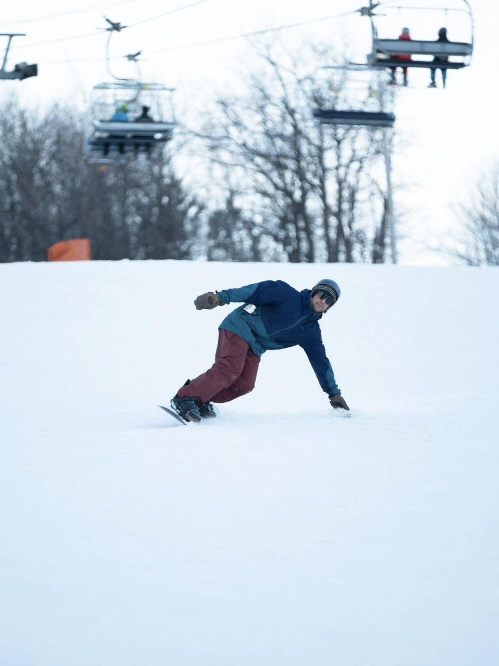 Snowboarder riding on snowy slope with ski lift in background.