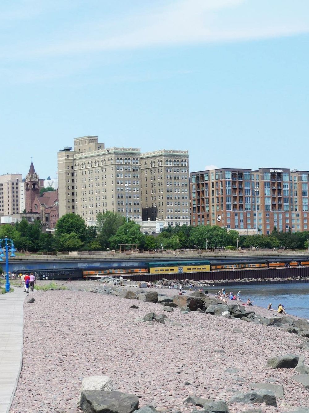 Downtown waterfront with parks, high-rise buildings, and a passenger train along the shoreline.