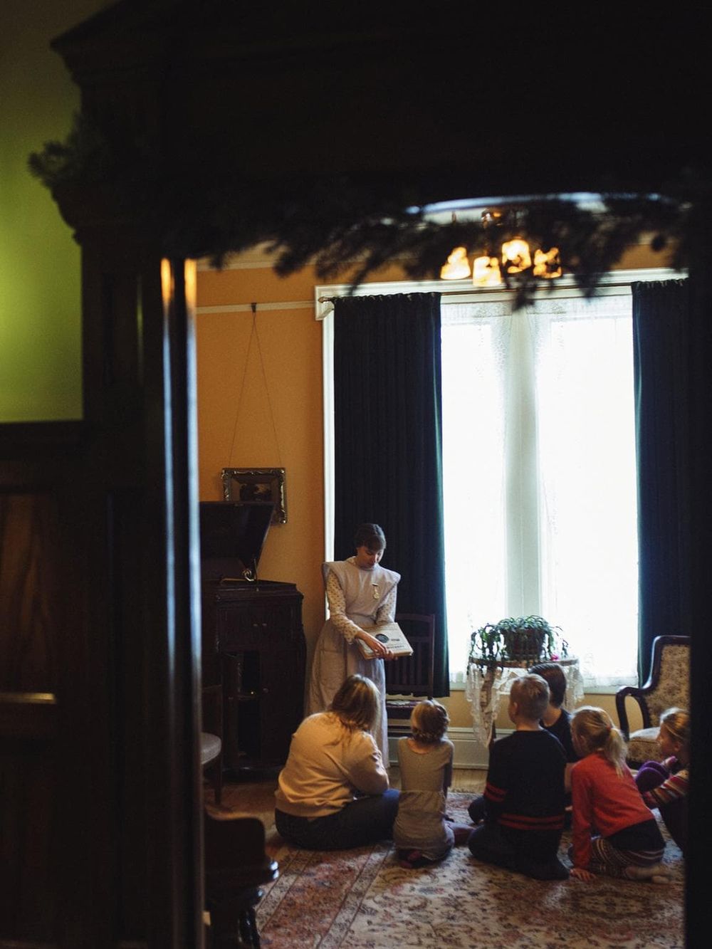 1. Vintage room with children and a woman reading story under soft natural light.