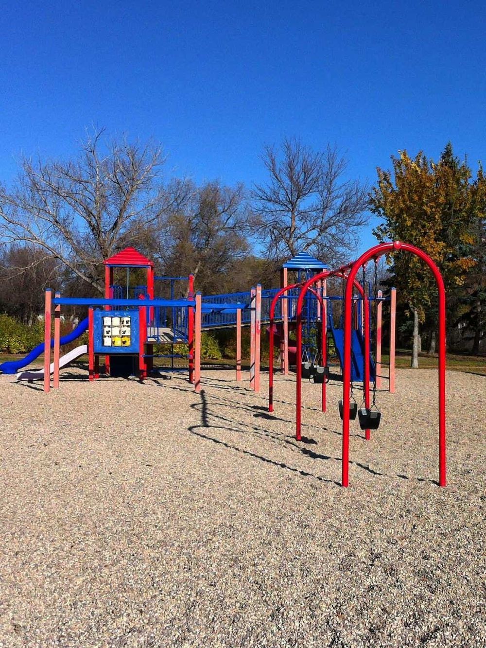 Colorful playground equipment with swings and slides at a park on a clear day.