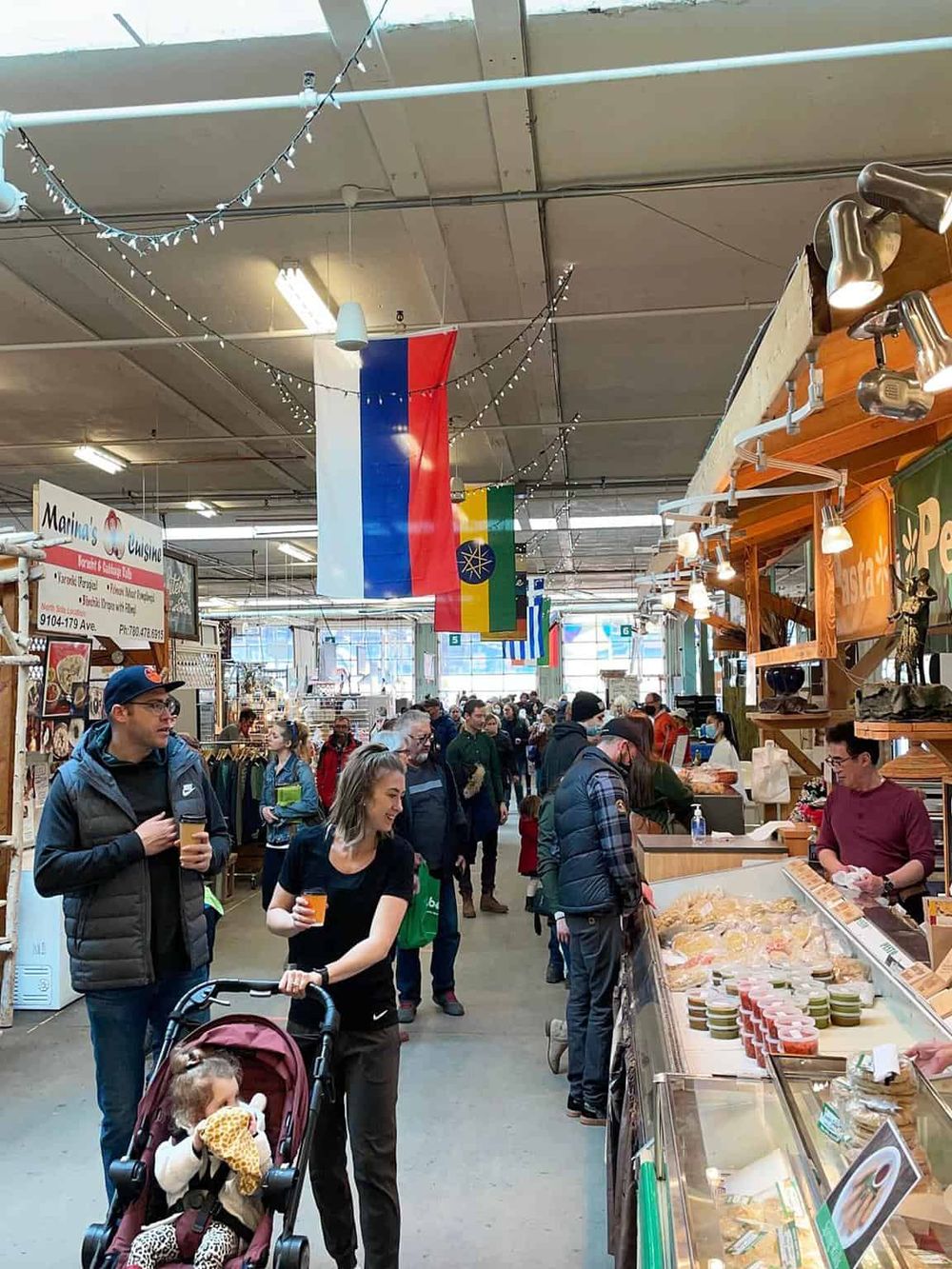 Colorful marketplace with diverse shoppers, flags, and food stalls, vibrant indoor scene of community gathering.