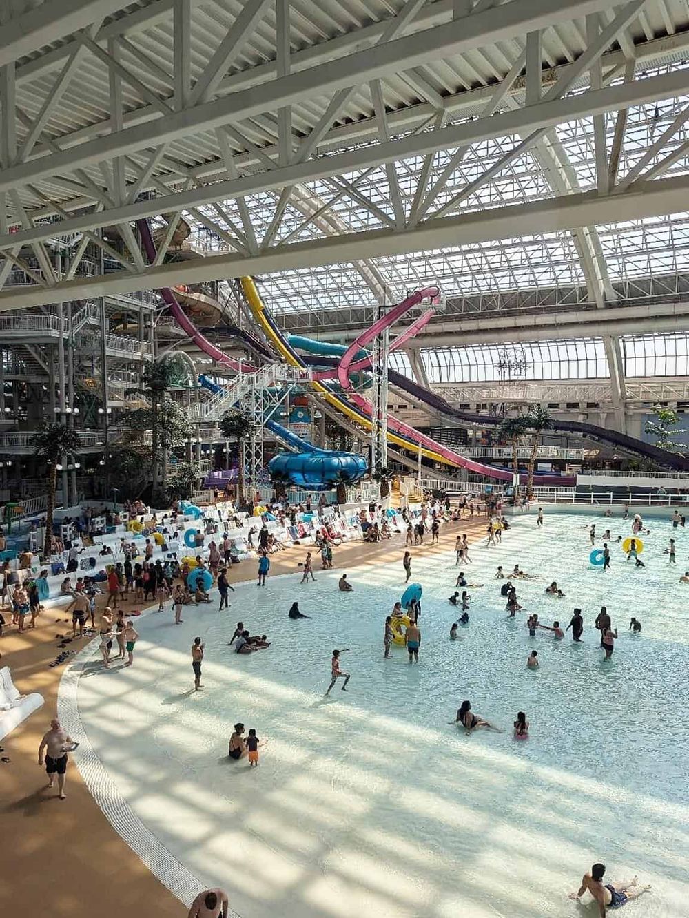 Indoor water park with multiple water slides and a large swimming area, bustling with visitors enjoying aquatic fun.
