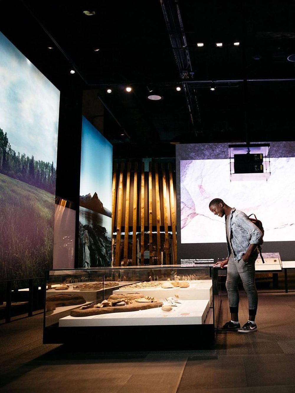 A person exploring a museum exhibit on nature and geography, engaging with displays of rocks and landscape photographs.