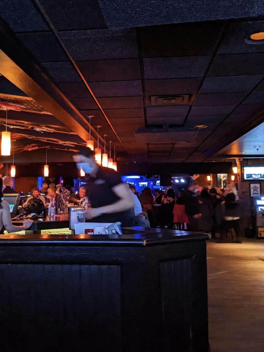 Dimly lit bar with patrons and servers, modern decor, and a lively social atmosphere.