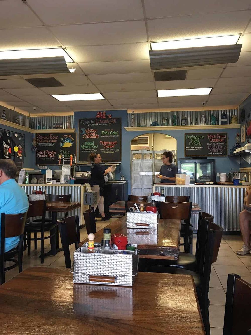 Coastal seafood restaurant interior with diners and chalkboard menu displaying fish and seafood dishes.