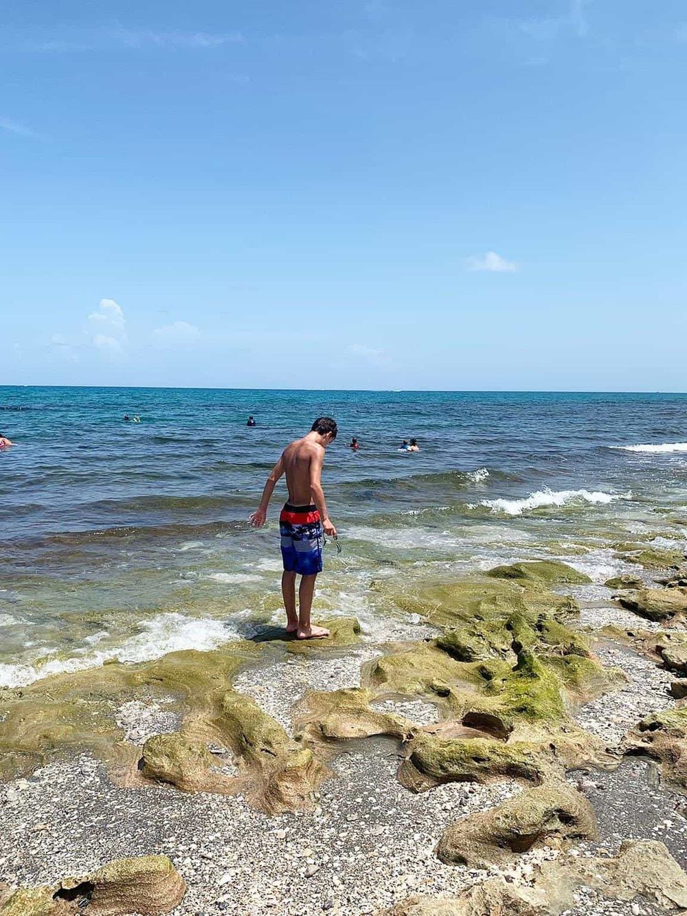 Kids enjoying beach and ocean water with rocky shoreline, sunny sky, and clear blue sea, perfect for beach vacation.