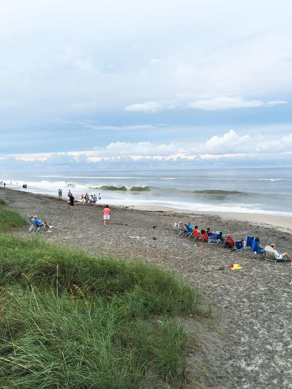 Sunny beach with lounge chairs and people enjoying the seaside, perfect for a relaxing vacation.