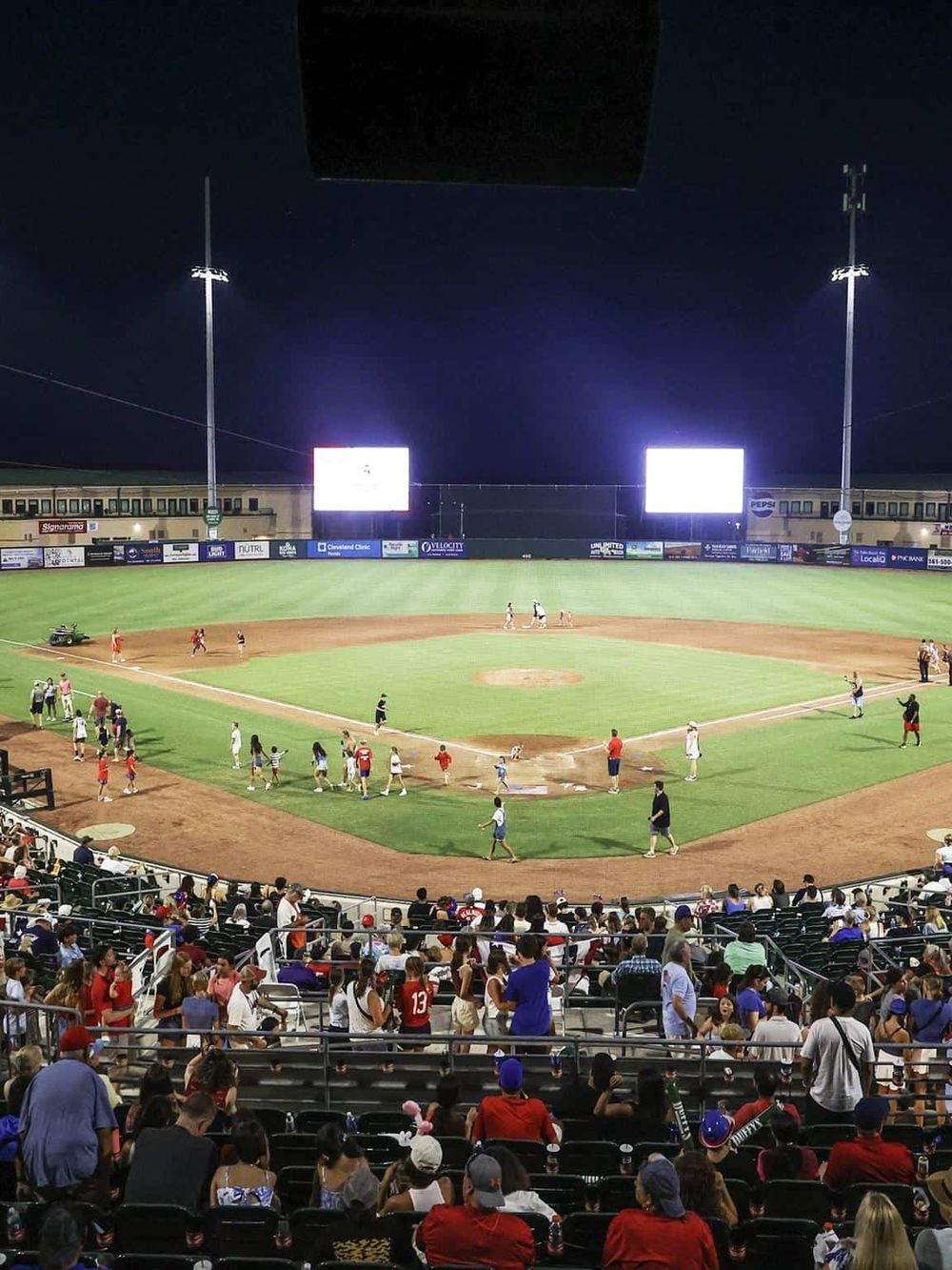 Brightly lit baseball stadium during night game with cheering crowd on stands.