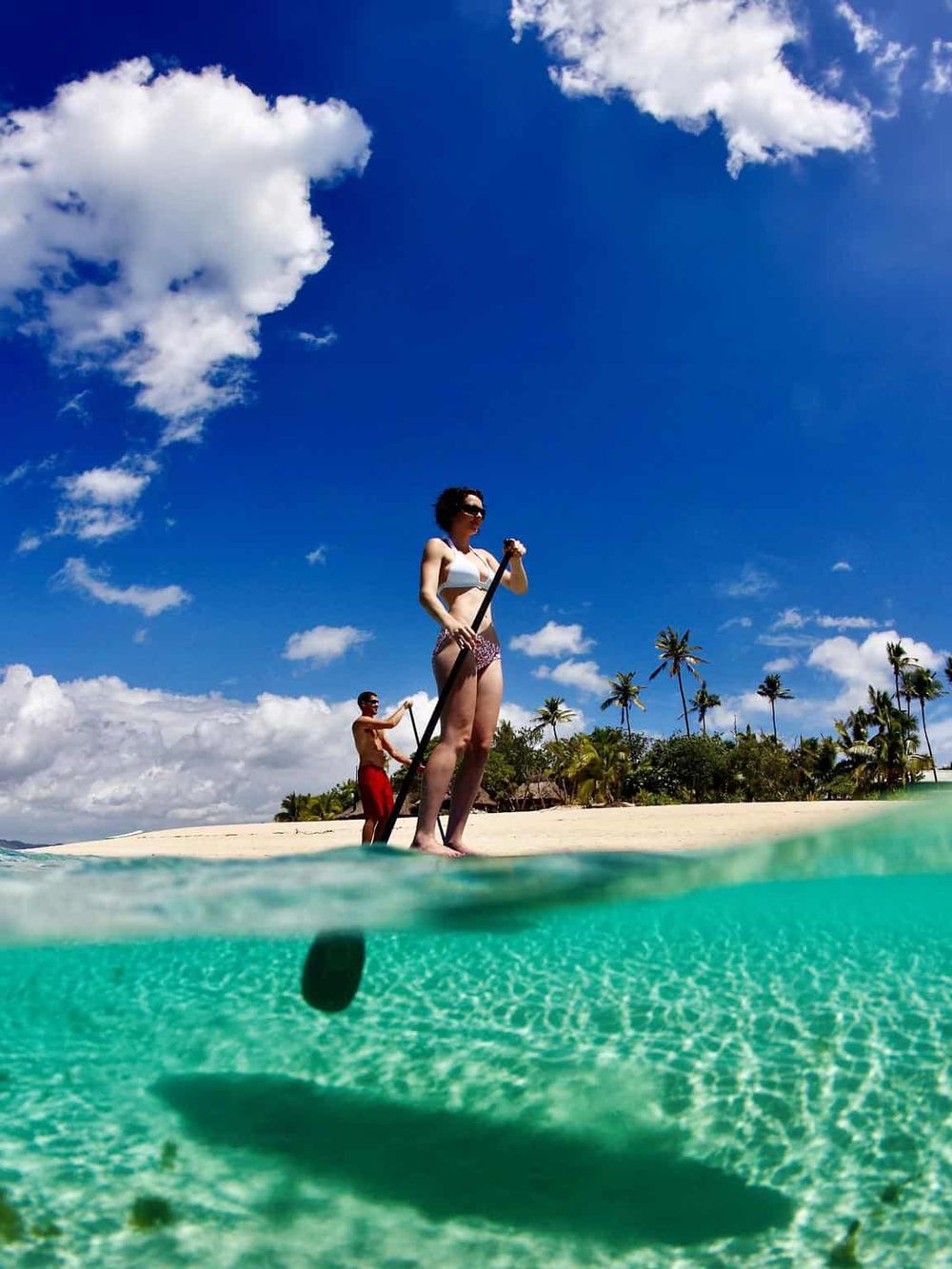 1. Women paddleboarding on clear tropical water under blue sky with palm trees.