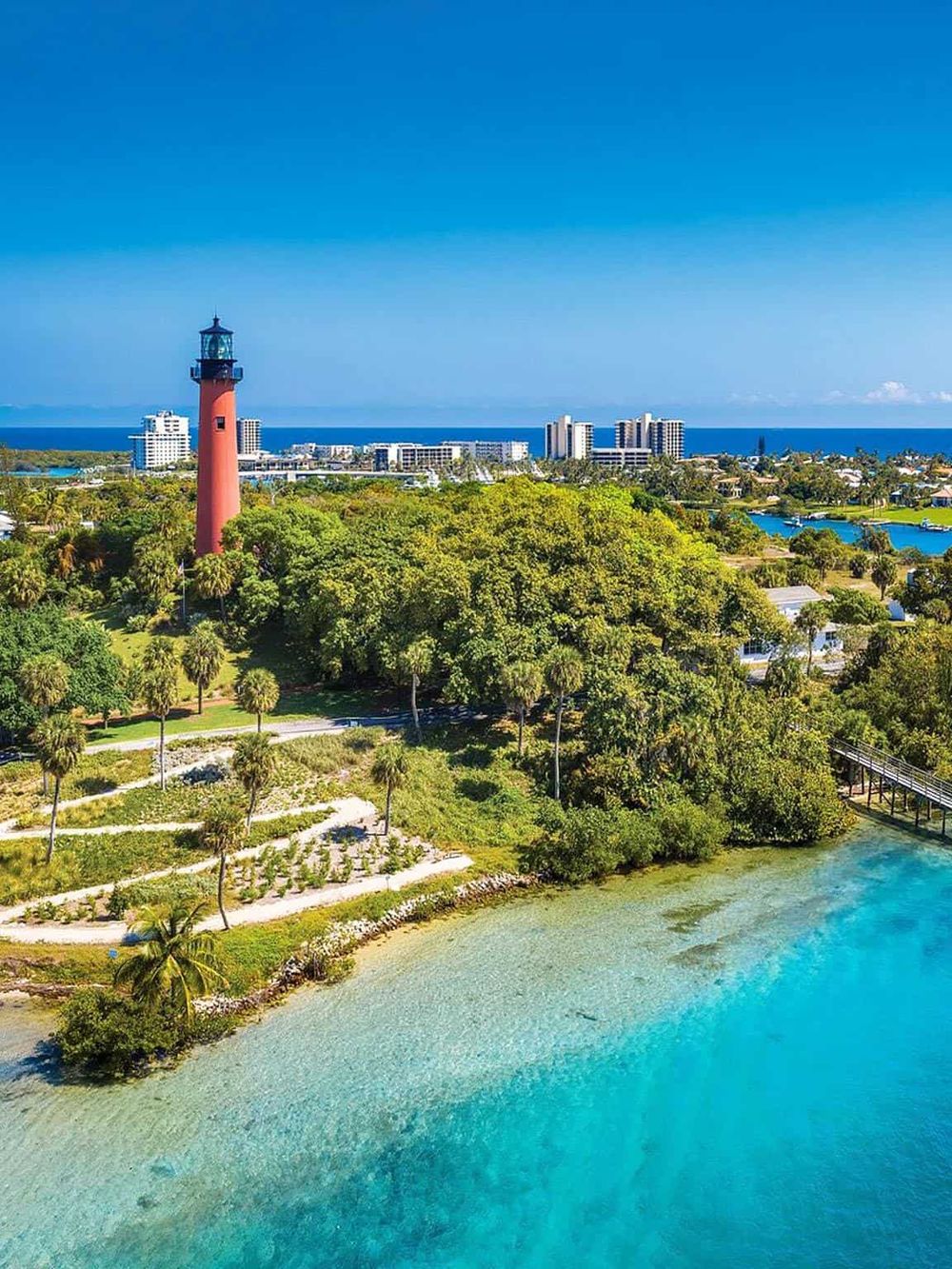 Colorful lighthouse overlooking lush greenery and clear turquoise waters in a scenic coastal landscape.