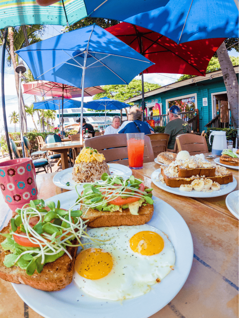 Colorful outdoor breakfast with sunny side eggs, toast, salad, and tropical drinks at a seaside café.