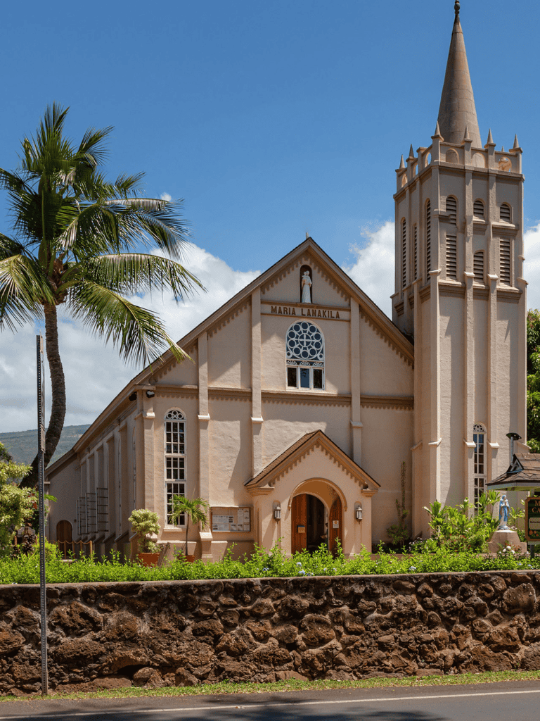 Seaside church with palm trees and clear blue sky, scenic Hawaiian landscape.