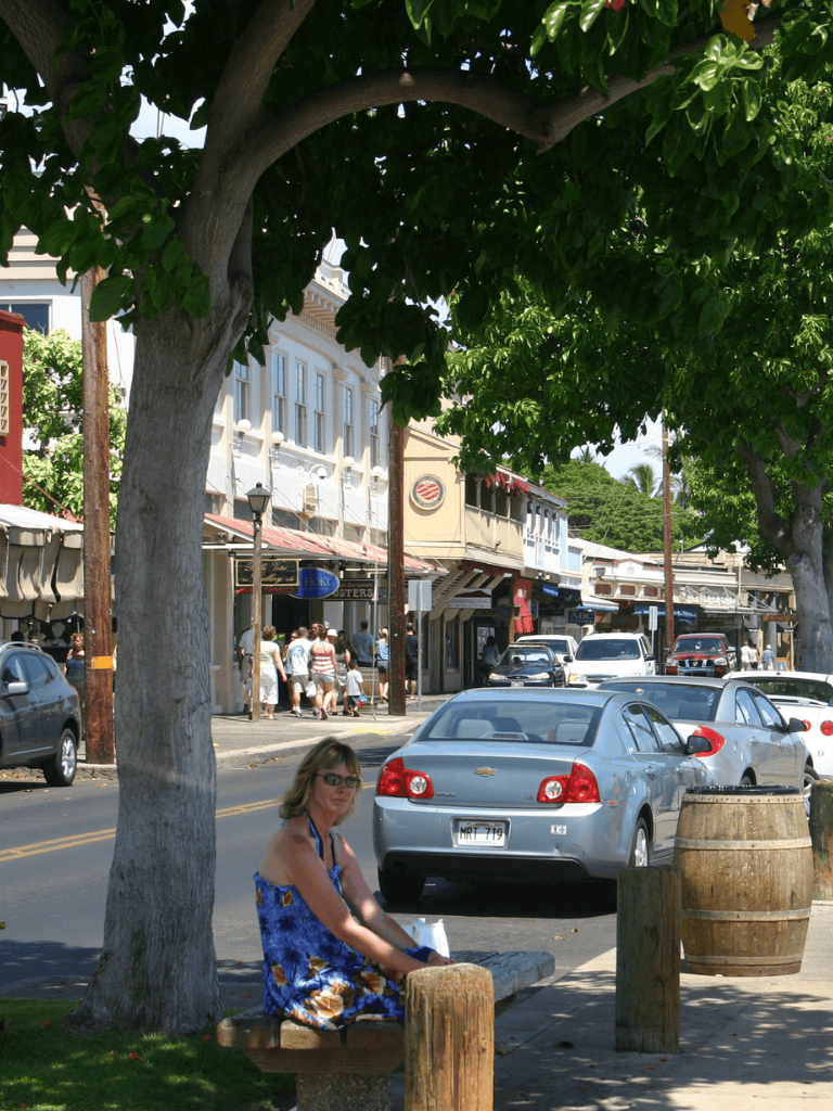 Relaxed woman sitting on park bench in downtown shopping district with cars and historic buildings.