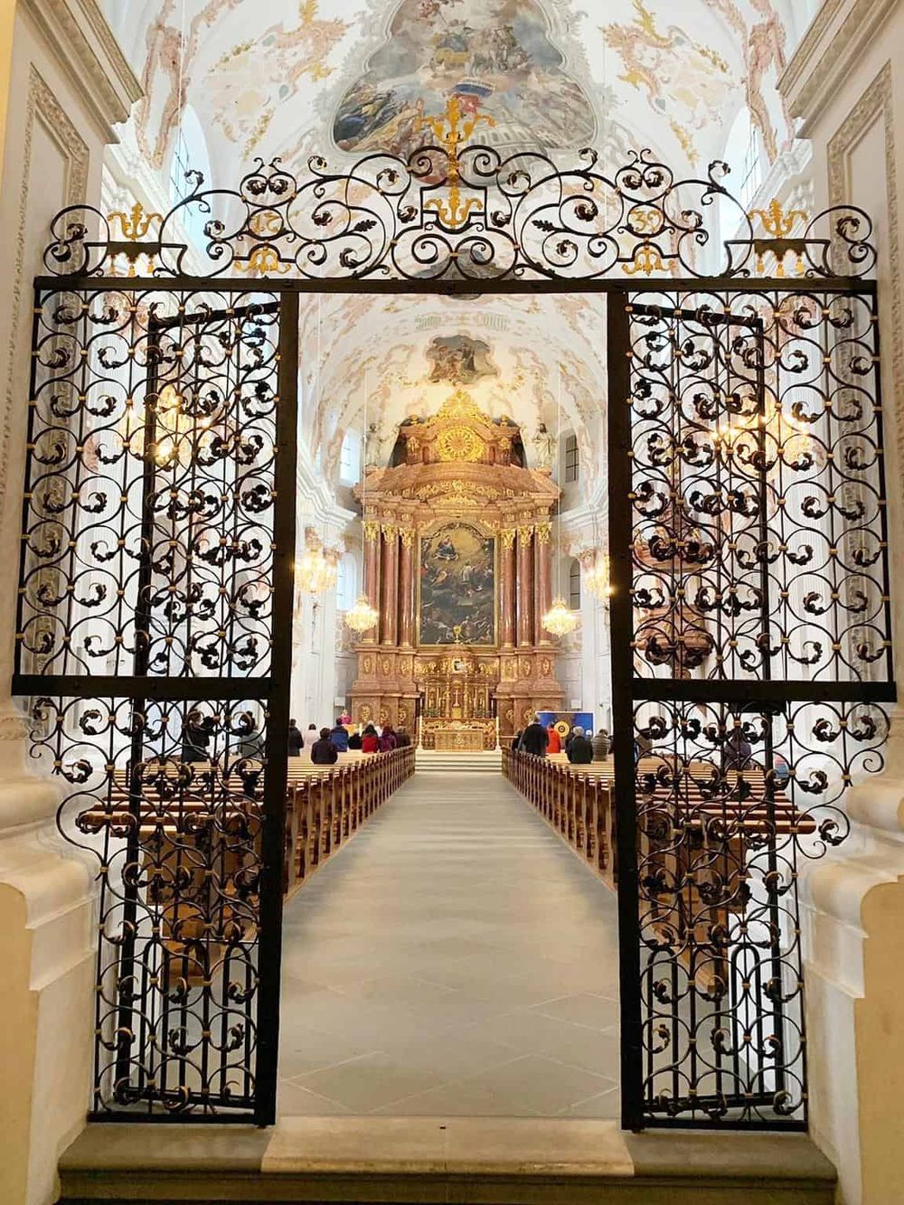 Intricate wrought iron gate opens to a stunning baroque church interior with gold accents and a large altar.