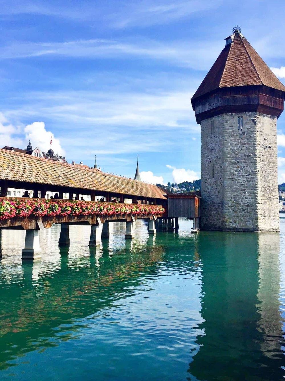Colorful medieval tower and wooden bridge over water at Chapel Bridge in Lucerne, Switzerland.