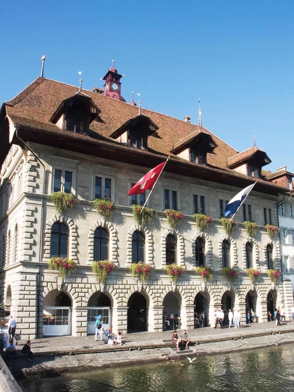 Historic Swiss town hall building with flags and flower boxes, located by the water in Switzerland.
