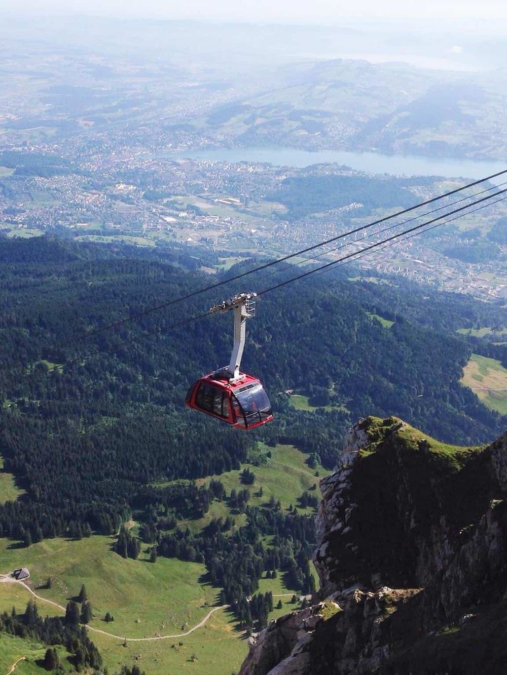 Aerial view of a cable car over lush green mountains with a scenic town below, emphasizing travel and adventure.