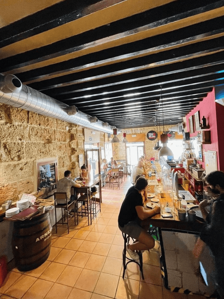 Cozy restaurant interior with stone walls, modern lighting, and customers dining at a bar and tables.